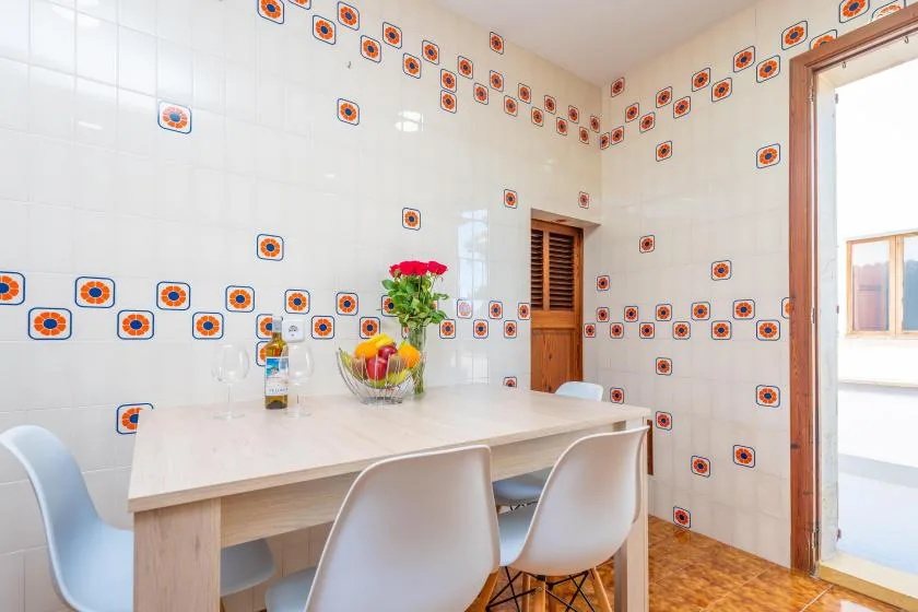 Comedor revestido de azulejos, con mesa, sillas y un pequeño arreglo floral.