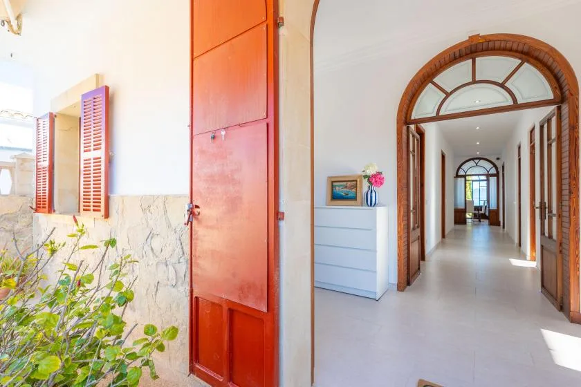 Un pasillo interior luminoso con arcos de madera y un pequeño mueble.