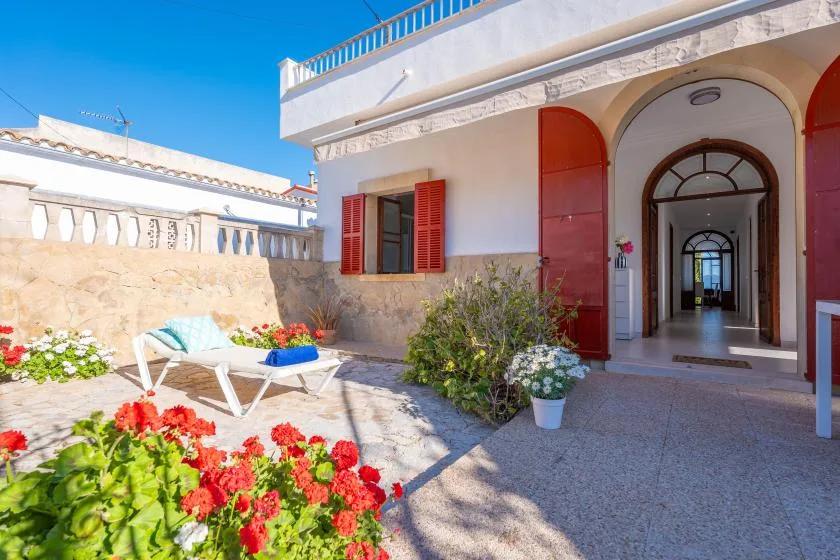 Un patio soleado con flores rojas, asientos al aire libre y una entrada con arco.