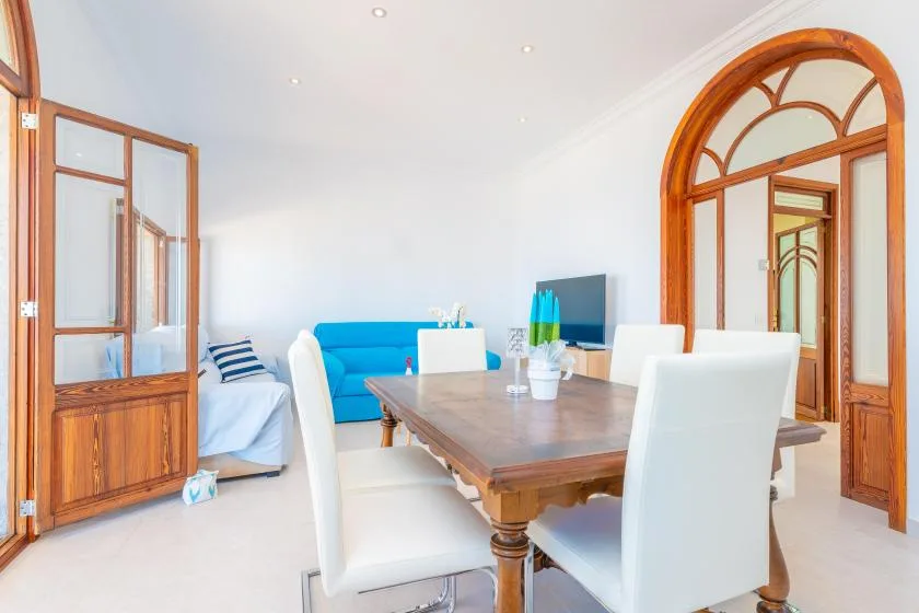 Un comedor luminoso con una mesa de madera y asientos blancos junto a un sofá azul.