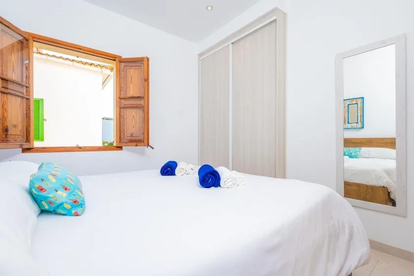 Un dormitorio luminoso con una cama bien tendida y una ventana de madera abierta.