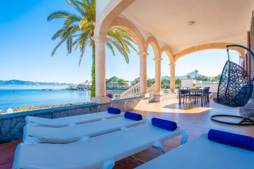 Una terraza cubierta frente al agua, con asientos, una mesa de comedor y vistas al mar.