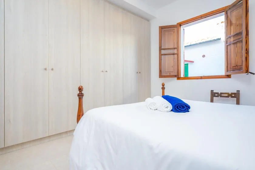 Un dormitorio luminoso con una cama, toallas dobladas y una ventana abierta.