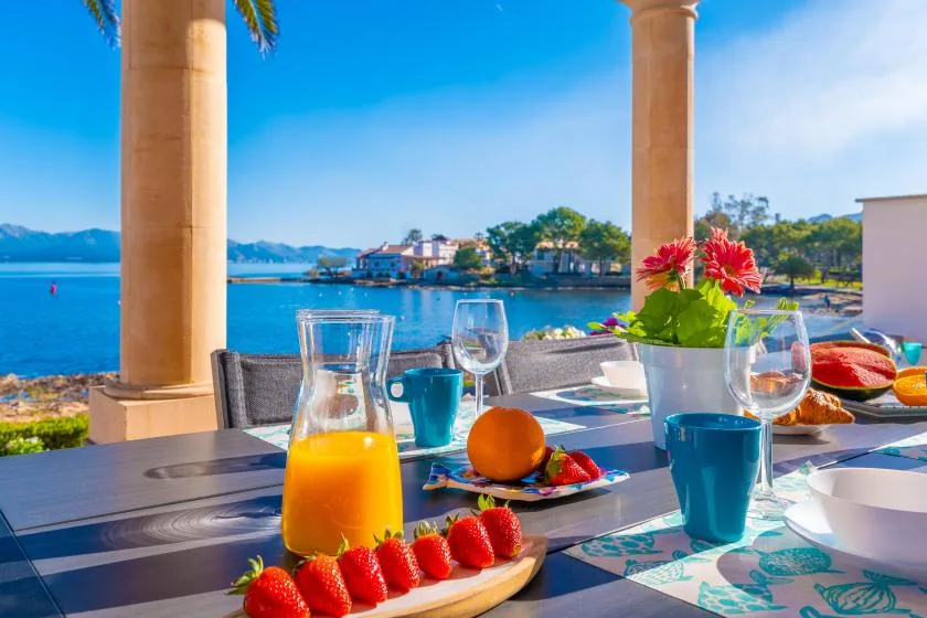 Una mesa junto al mar está preparada con desayuno, flores y vistas al agua.