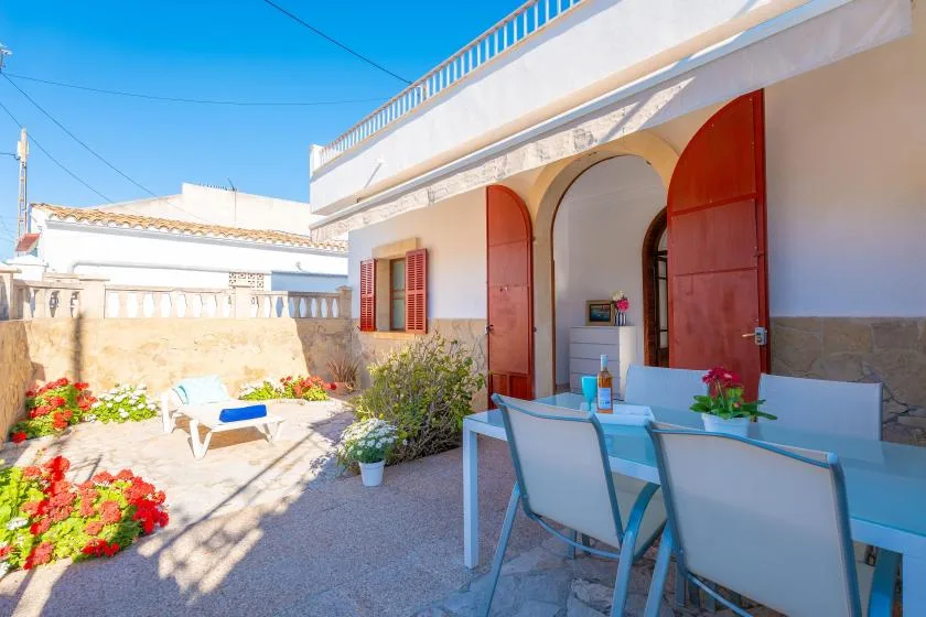 Una zona de comedor al aire libre está junto a un edificio blanco con puertas rojas abiertas.