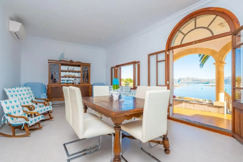 Comedor luminoso con una mesa de madera y una puerta arqueada de vidrio con vista al agua.