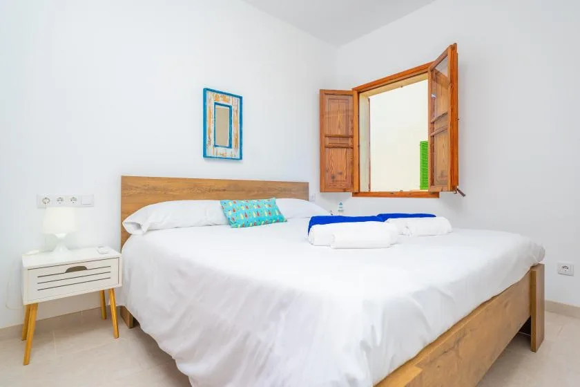Un dormitorio luminoso con una cama bien hecha bajo una ventana de madera abierta.