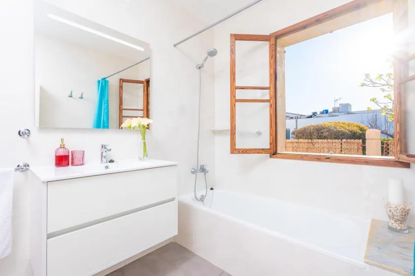 Un baño luminoso con bañera, ducha y lavabo junto a una ventana abierta.