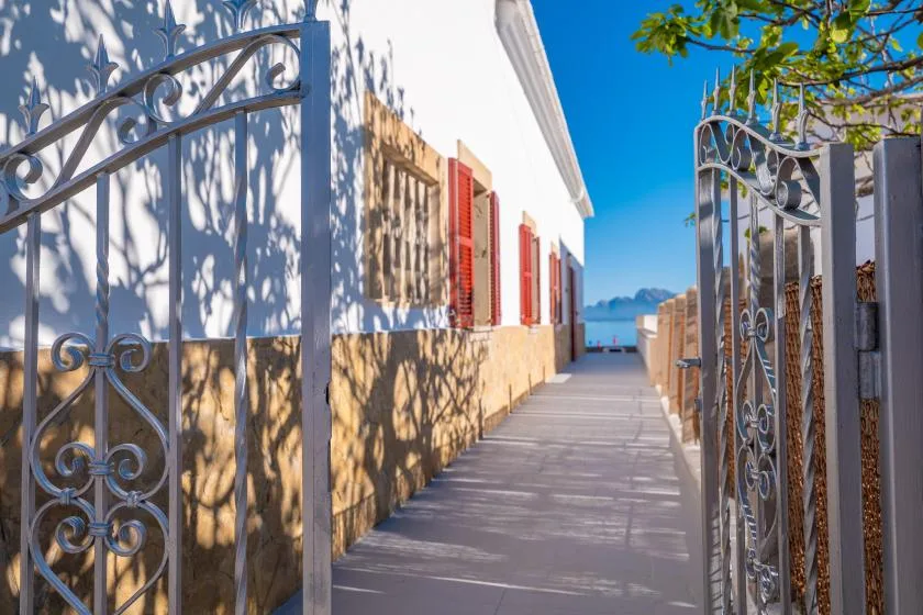 Una puerta abierta da a un sendero soleado junto a un edificio blanco.
