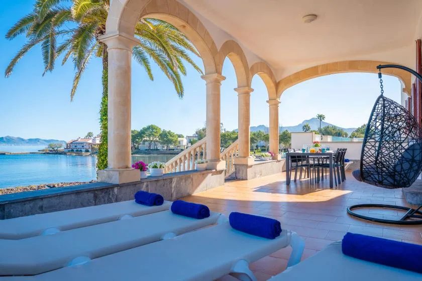 Una terraza cubierta da al agua, con asientos y una silla colgante.
