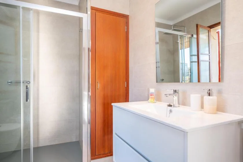 Un baño luminoso con una ducha de vidrio y un lavabo blanco.