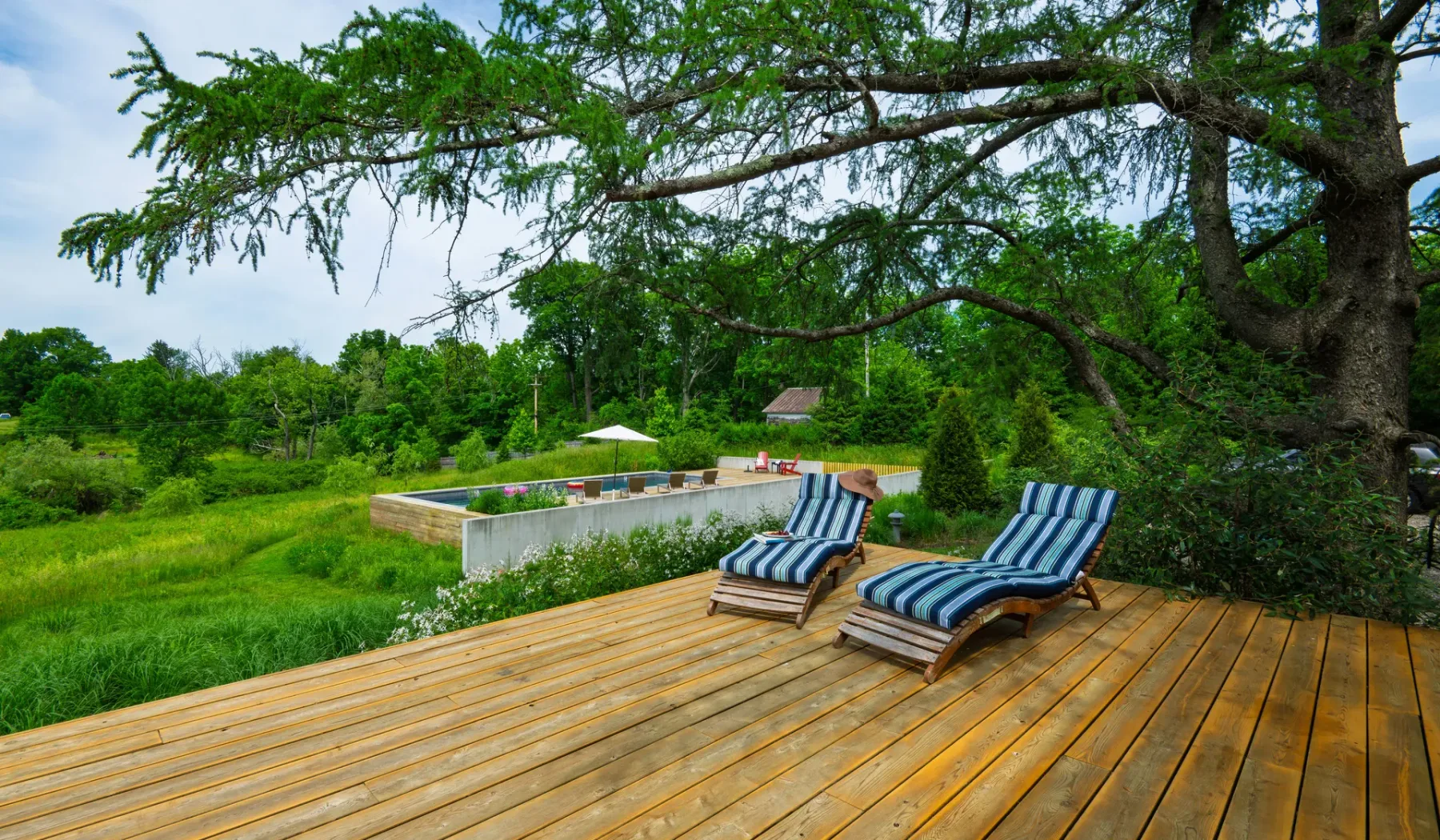 Una terraza de madera con dos tumbonas a rayas da a un paisaje verde.