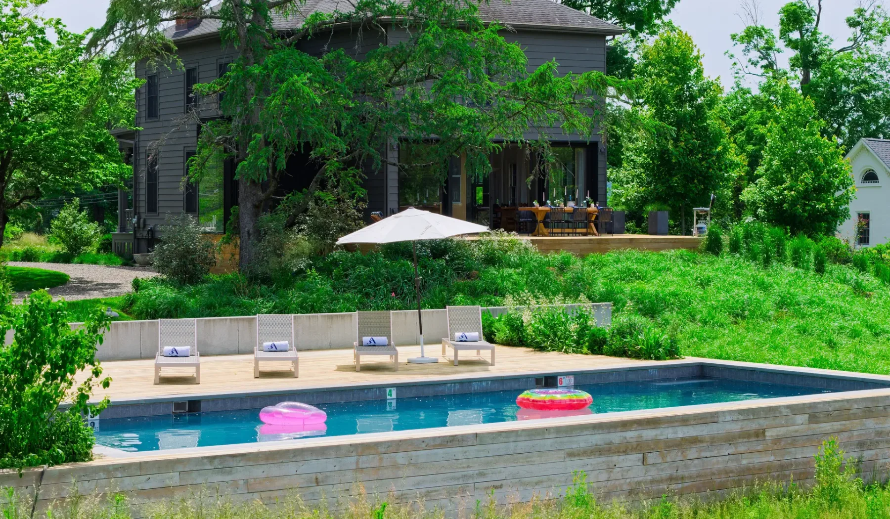 Piscina al aire libre junto a una casa moderna, con tumbonas junto a la terraza.