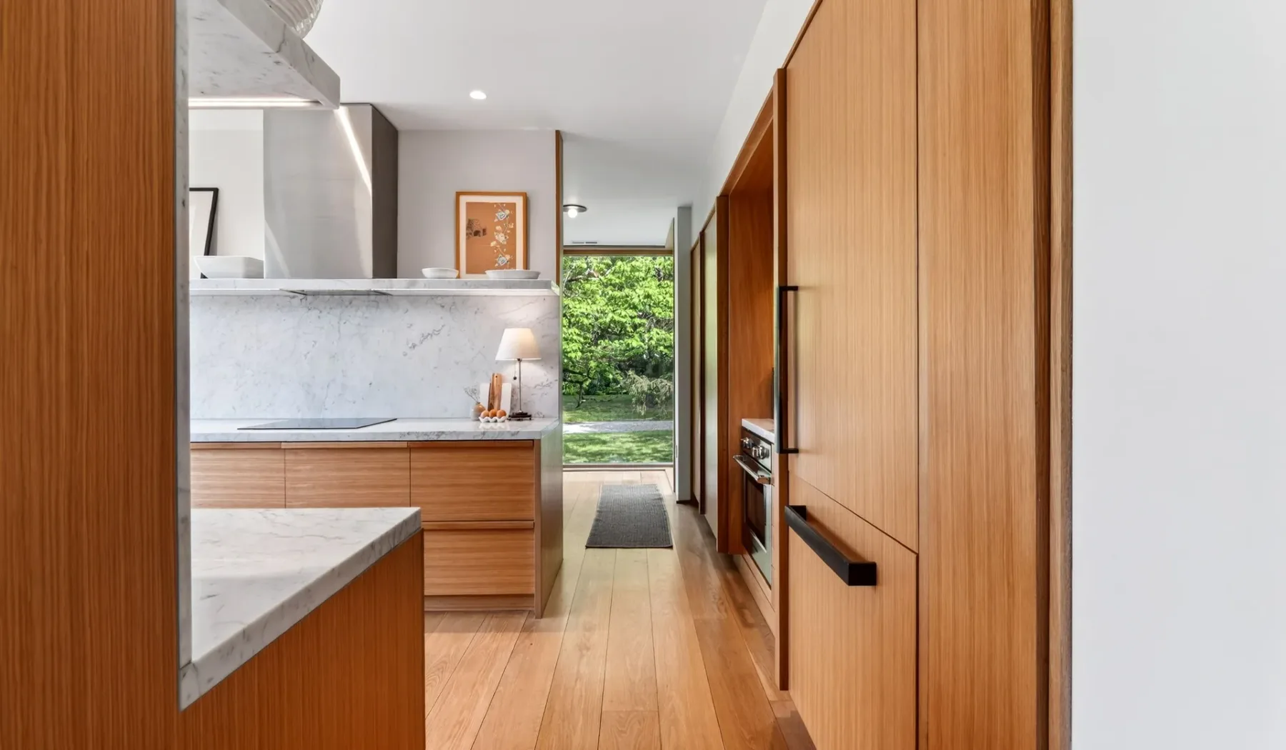 Una cocina moderna con gabinetes de madera y vegetación visible por la ventana.