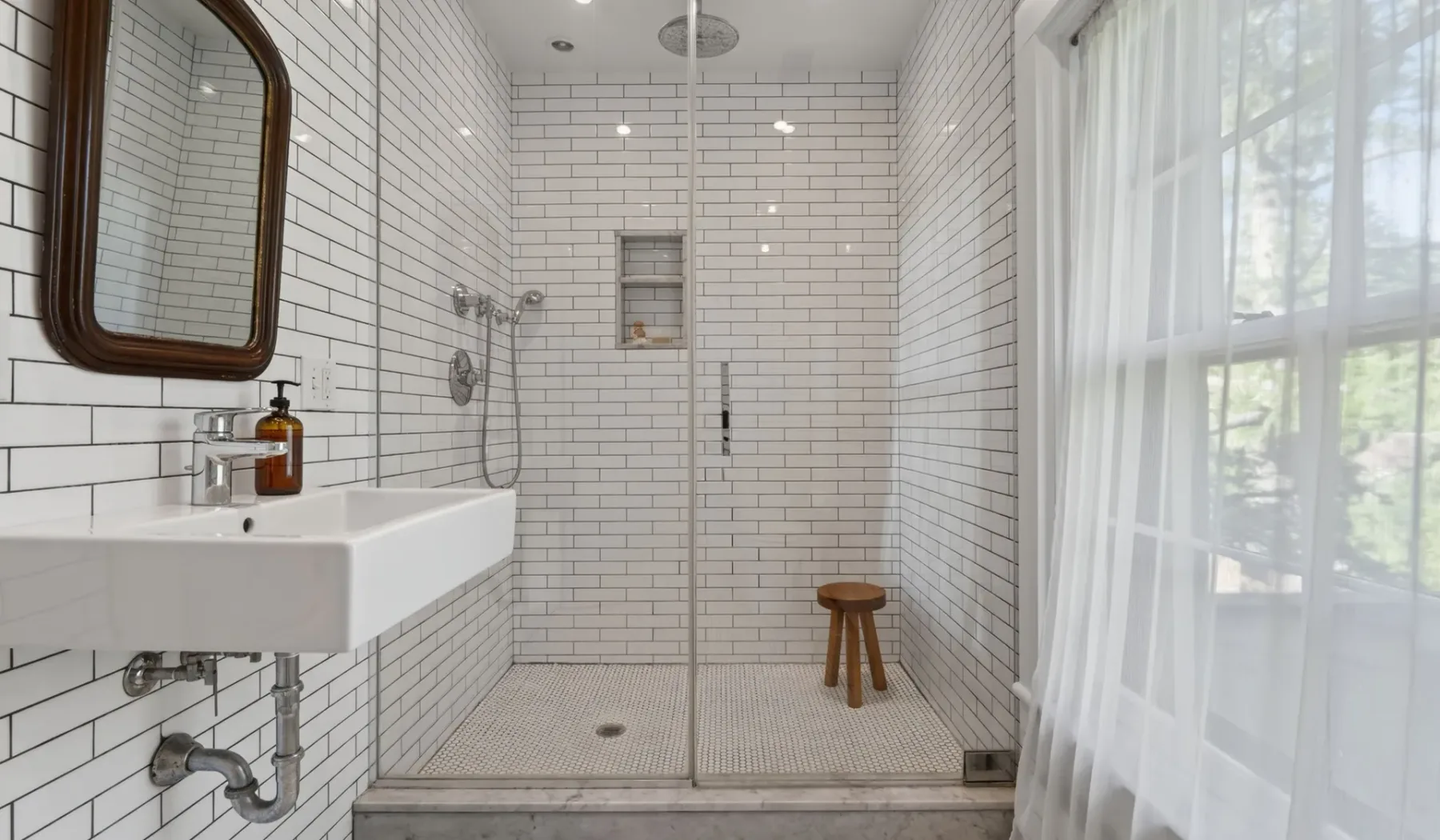 Un baño luminoso con azulejos, un lavabo de pared y una ducha de vidrio.