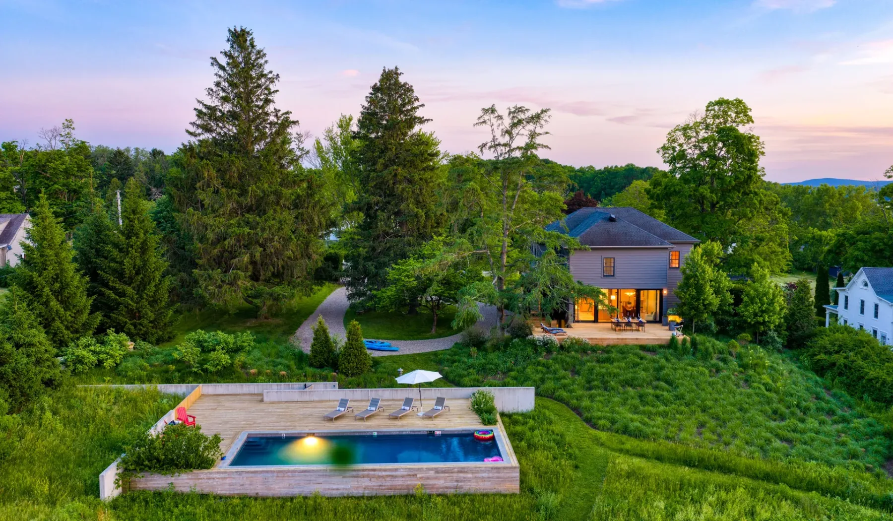 Una casa y una piscina al aire libre se encuentran entre árboles y jardines al anochecer.