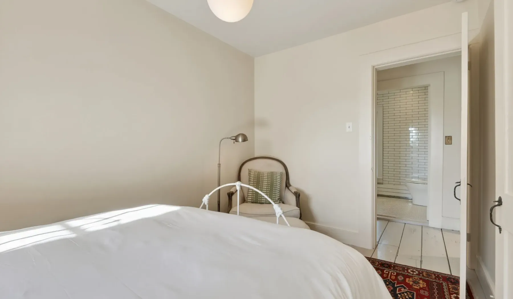 Un dormitorio con una cama bien tendida y una silla junto a la pared.