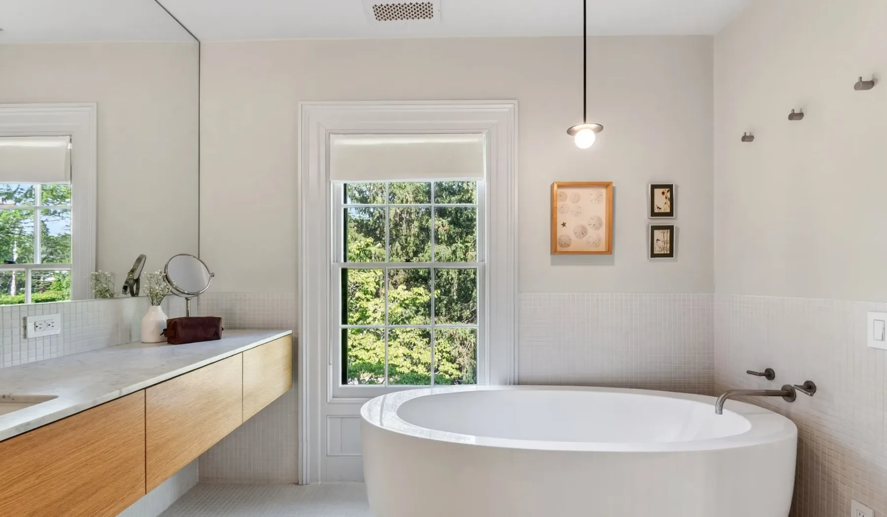 Un baño luminoso con una bañera exenta y una ventana grande.