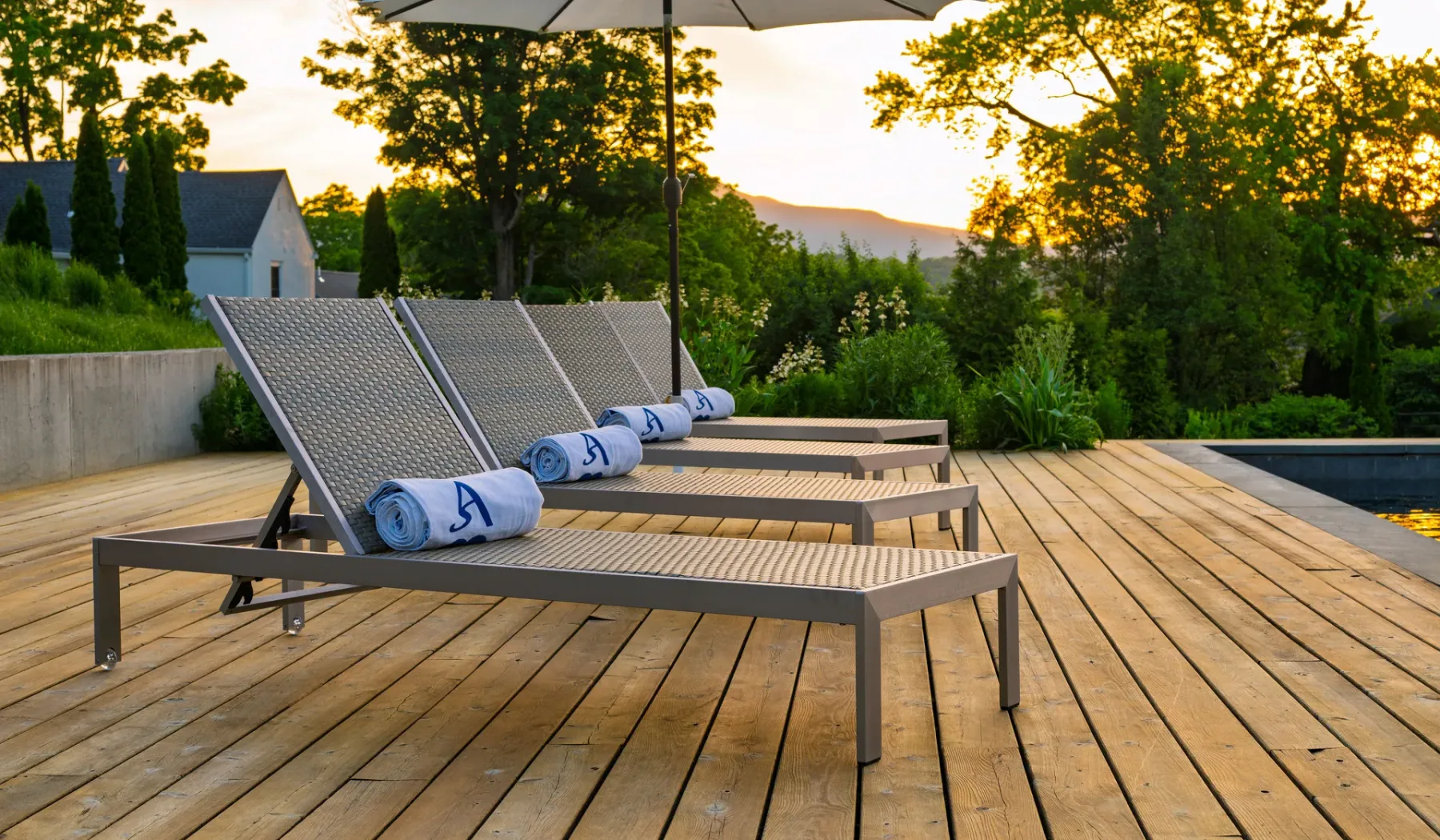 Terraza exterior con asientos reclinables y toallas enrolladas junto a una piscina.