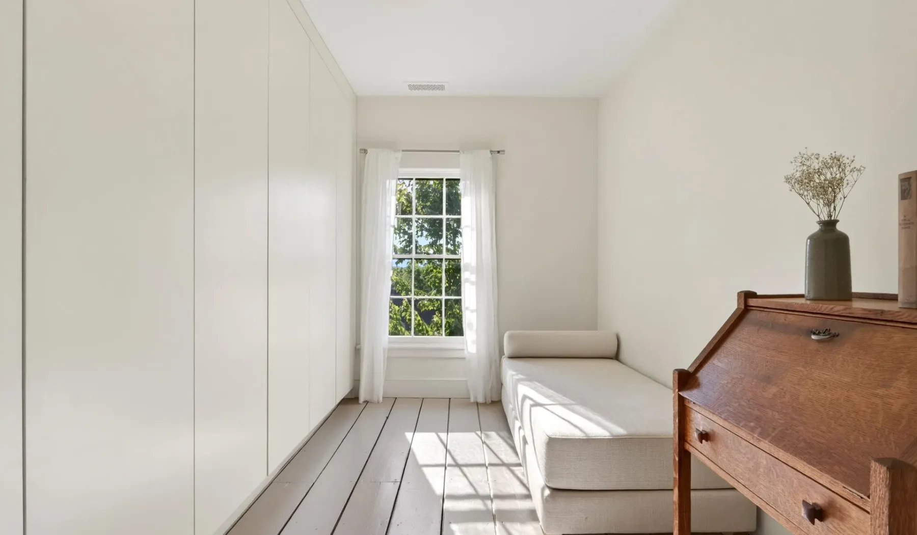 Una zona de estar luminosa con una ventana, asientos claros y un escritorio de madera.