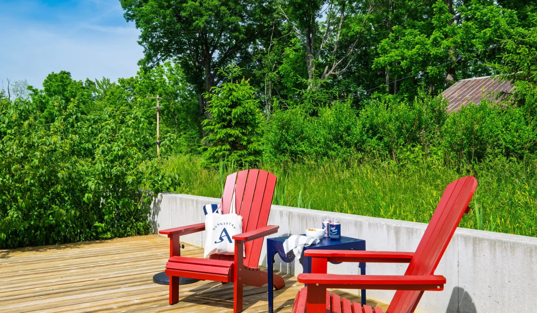 Una terraza de madera con asientos rojos da a árboles y arbustos frondosos.