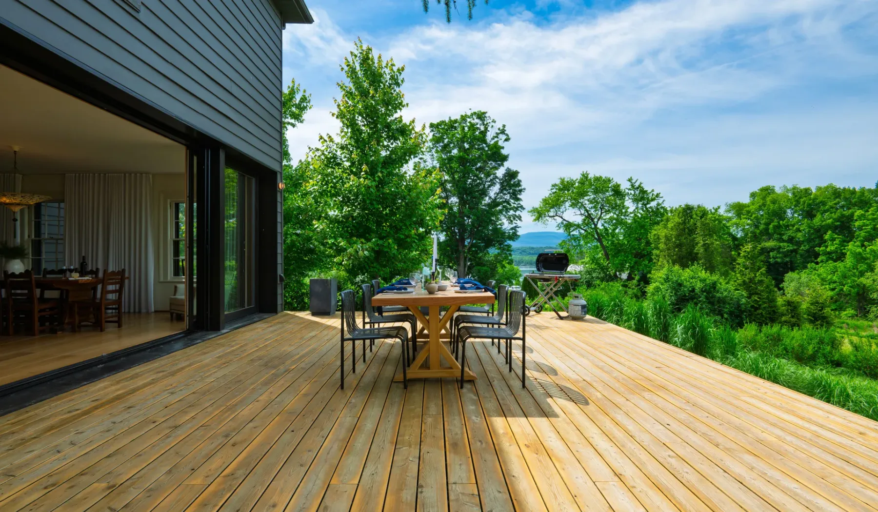 Una terraza de madera con asientos para comer al aire libre da a un paisaje frondoso.