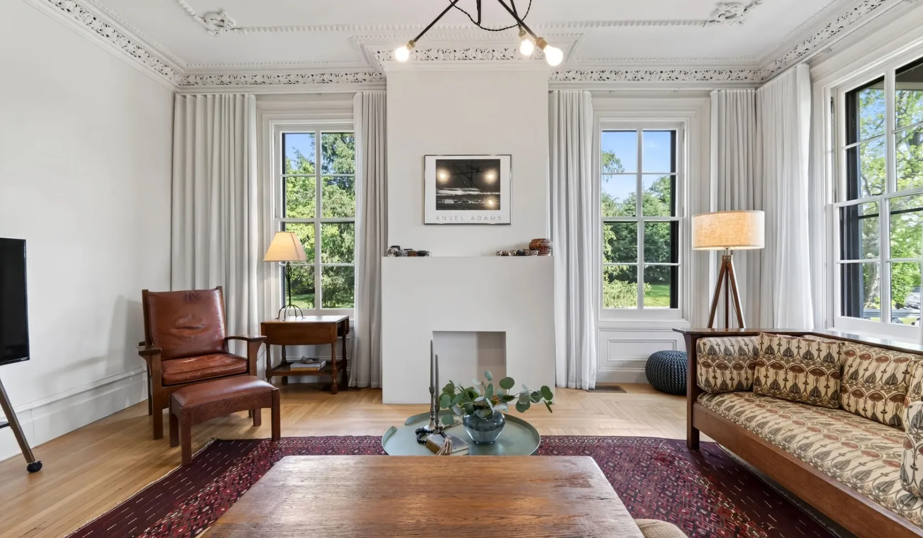 Una sala de estar luminosa con ventanas altas, una chimenea y asientos alrededor de una mesa de centro.