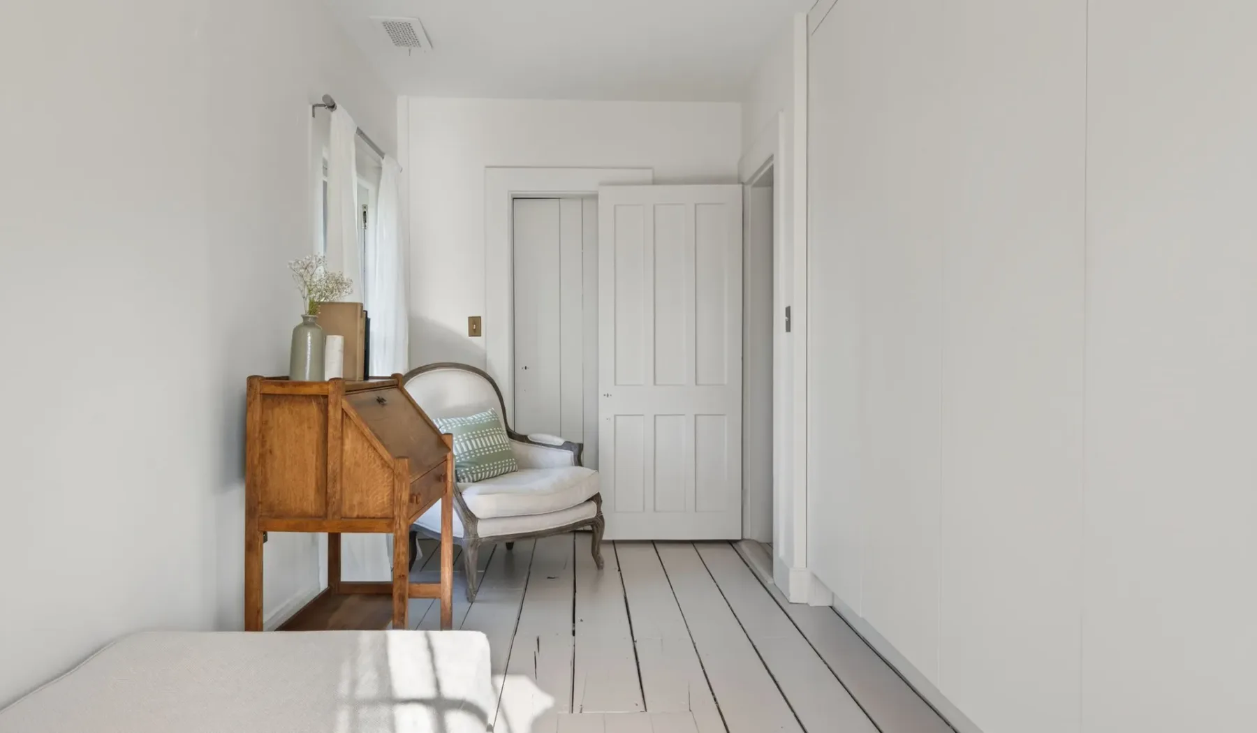 Una habitación luminosa con un escritorio de madera, asientos y una puerta blanca con paneles.