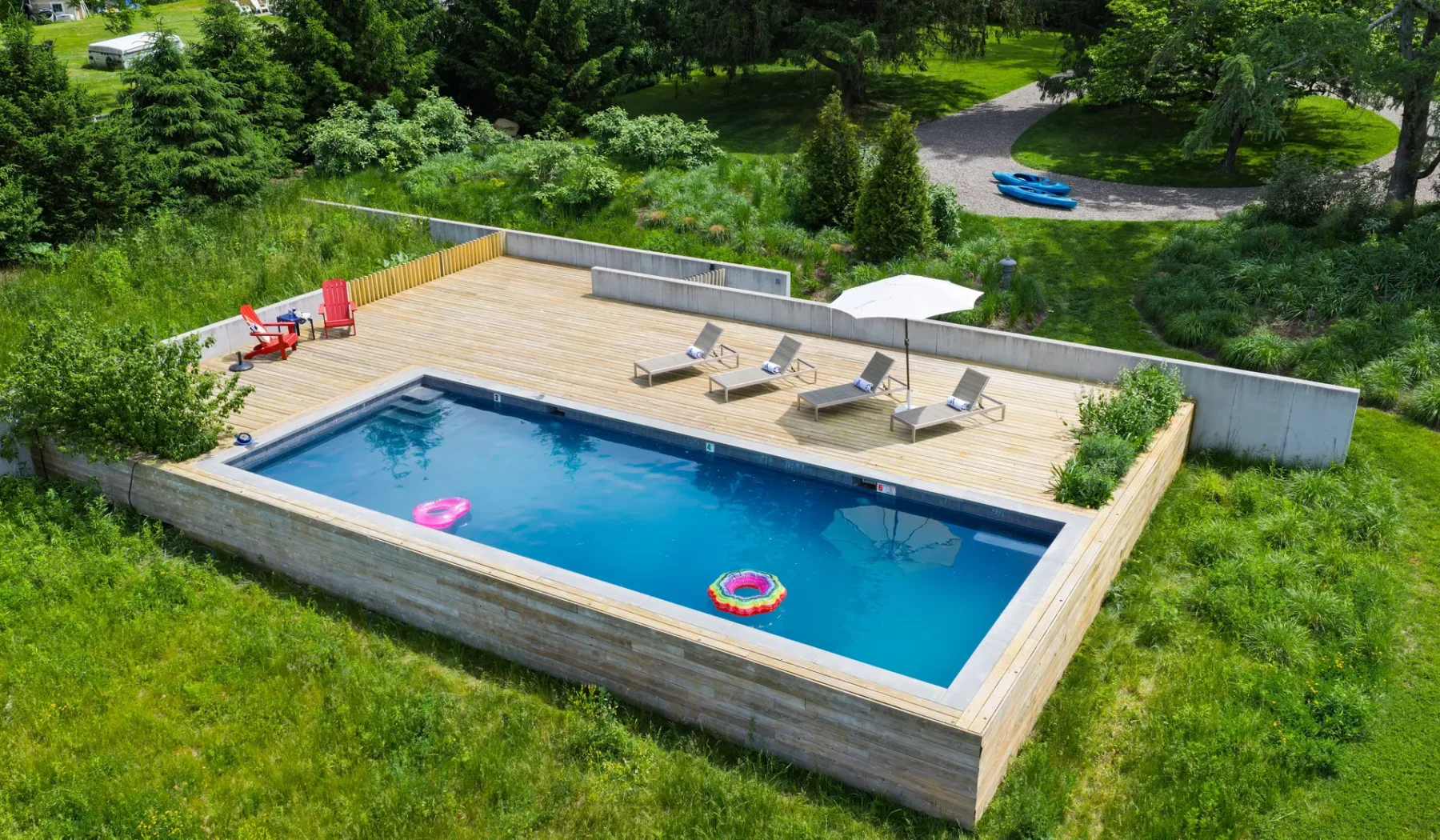 Una piscina al aire libre está junto a una terraza de madera con asientos.