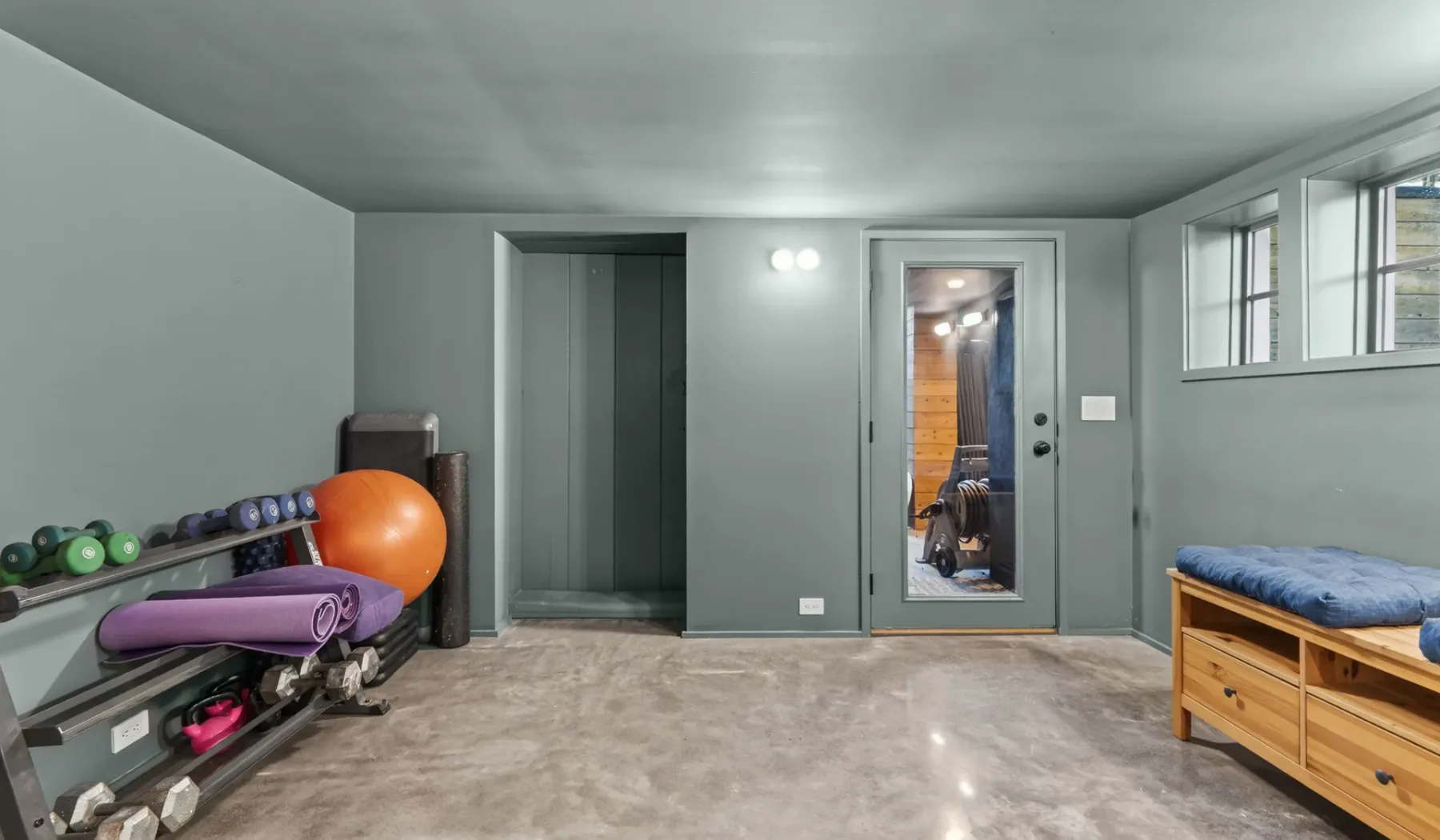 Un gimnasio en el sótano con equipo de ejercicio y un banco acolchado.