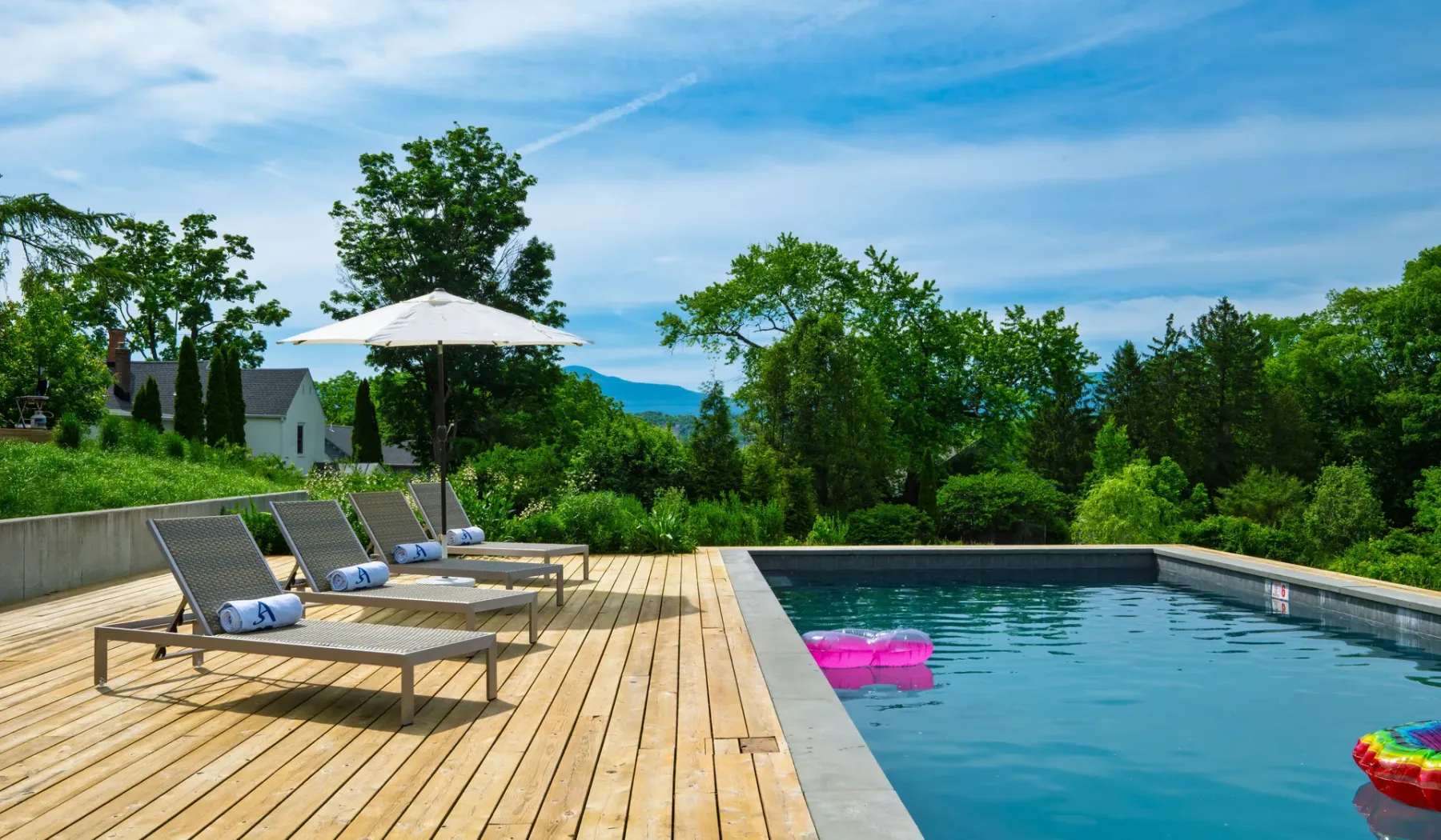 Una piscina al aire libre junto a una terraza de madera con asientos y una sombrilla.