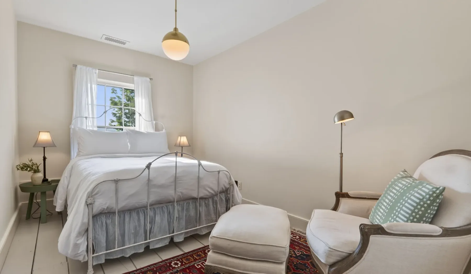 Dormitorio con una cama bien tendida y un sillón tapizado a un lado.