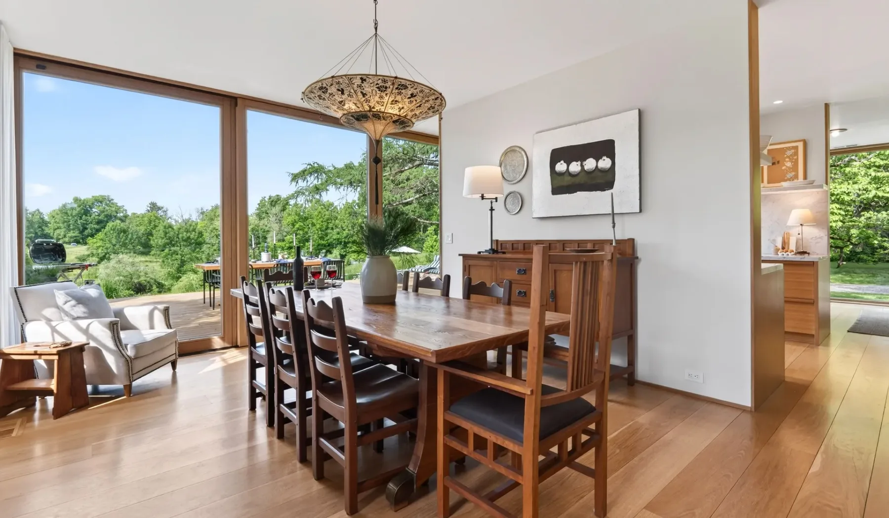 Un comedor con una larga mesa de madera junto a grandes ventanales con vistas a la vegetación.