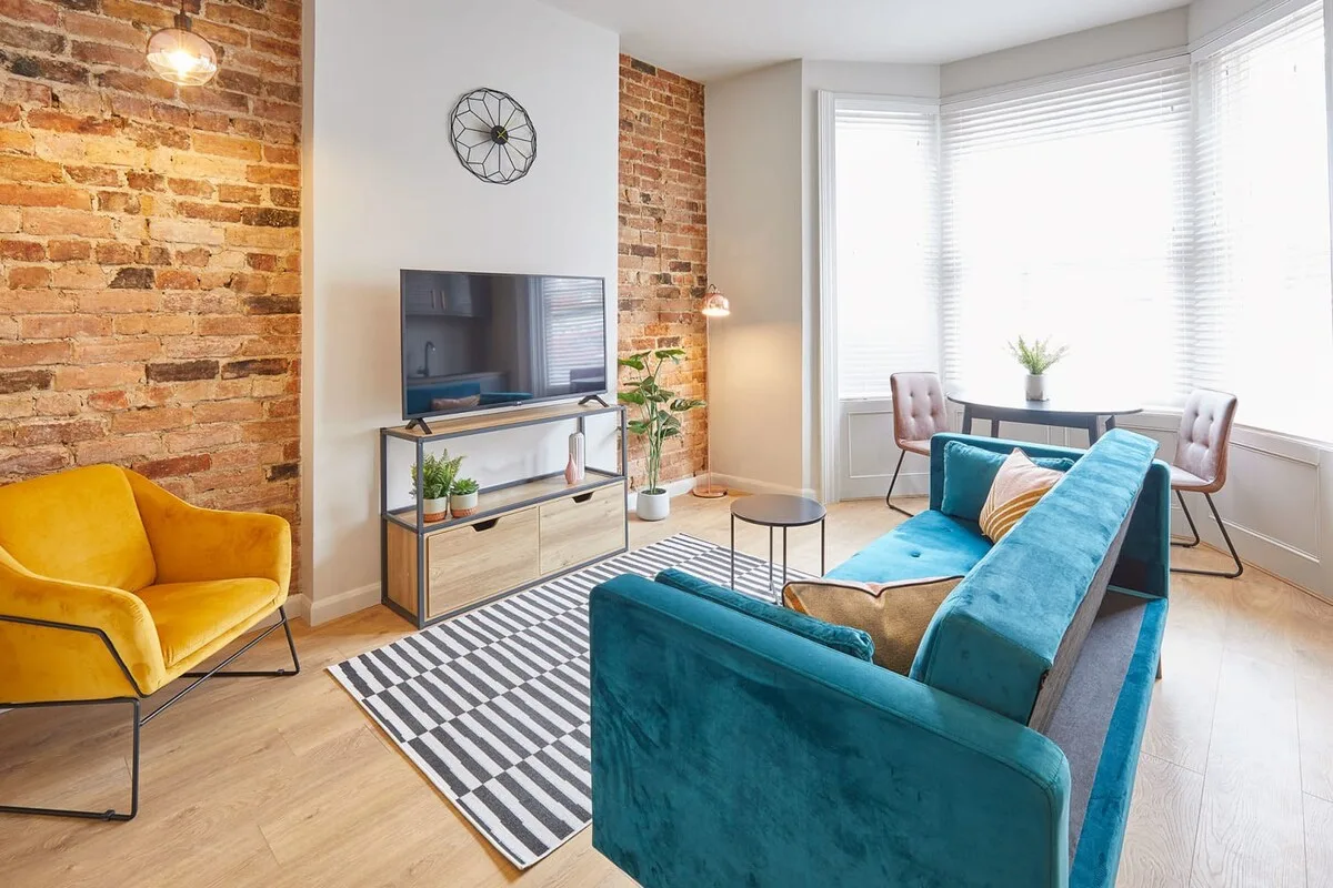 A bright living room with teal seating, a television, and large windows.