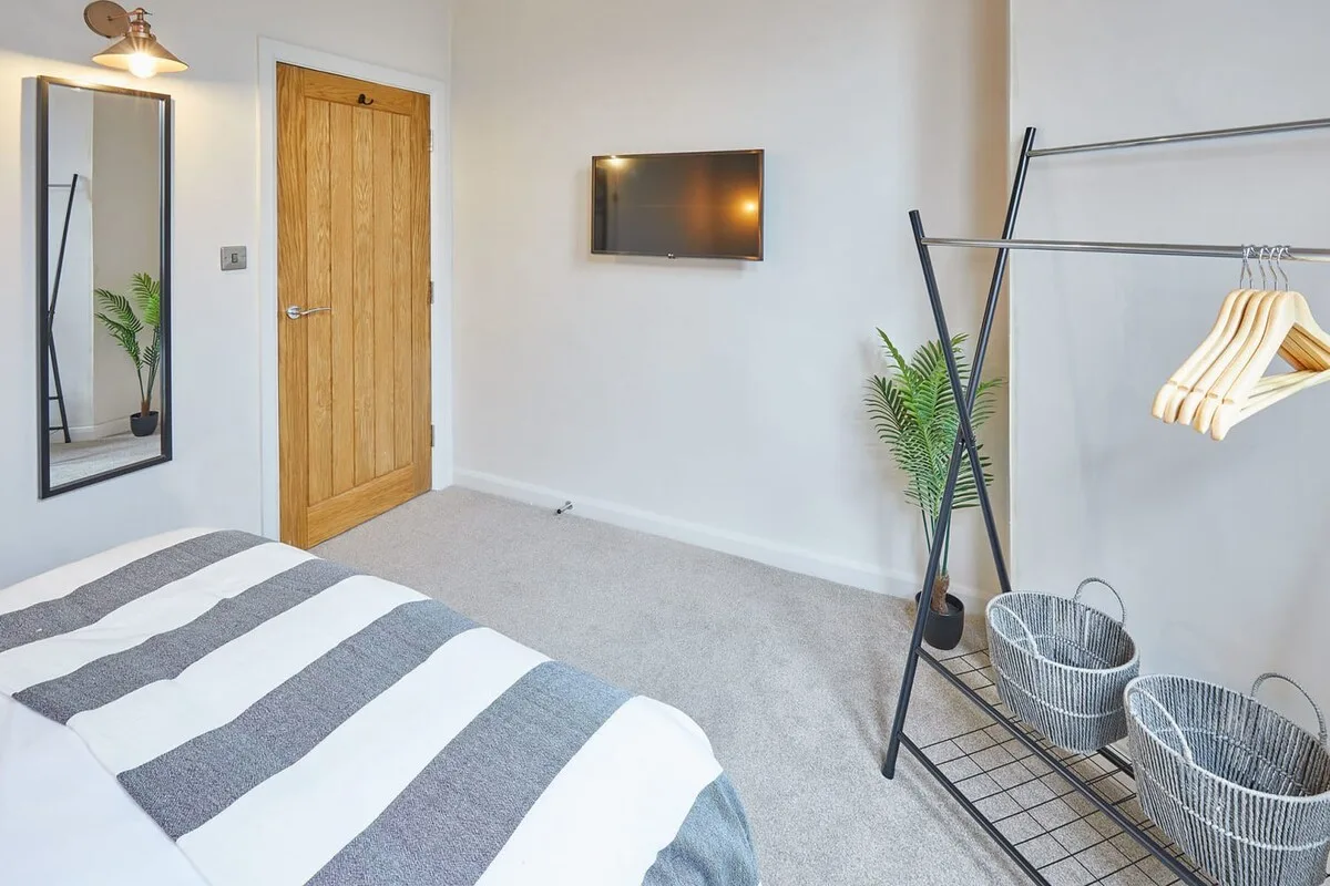 A bedroom with a striped bedspread, wall-mounted television, and freestanding clothing rack.