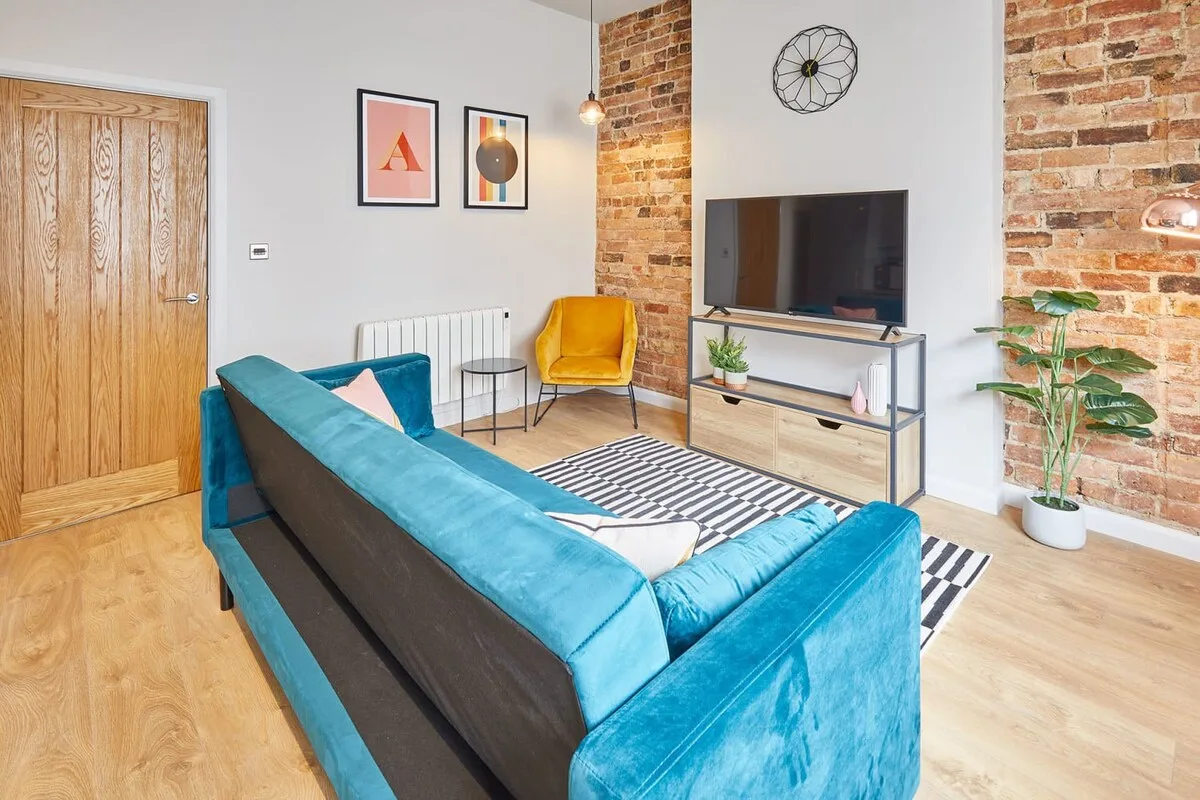 A living room with a teal sofa, television, and exposed brick walls.