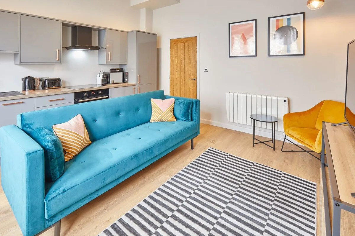 An open-plan living room and kitchen with a blue sofa and striped rug.