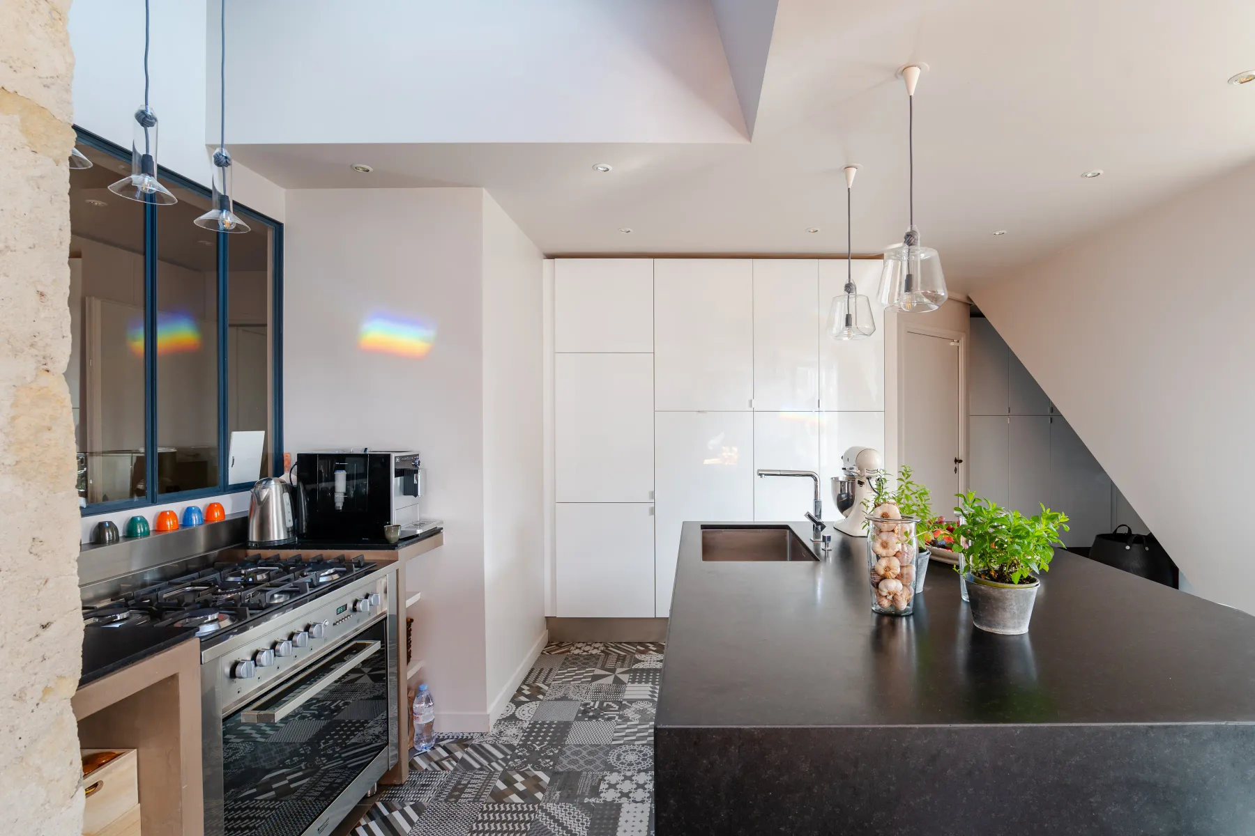 A modern kitchen with a long island, cooking range, and potted plants.