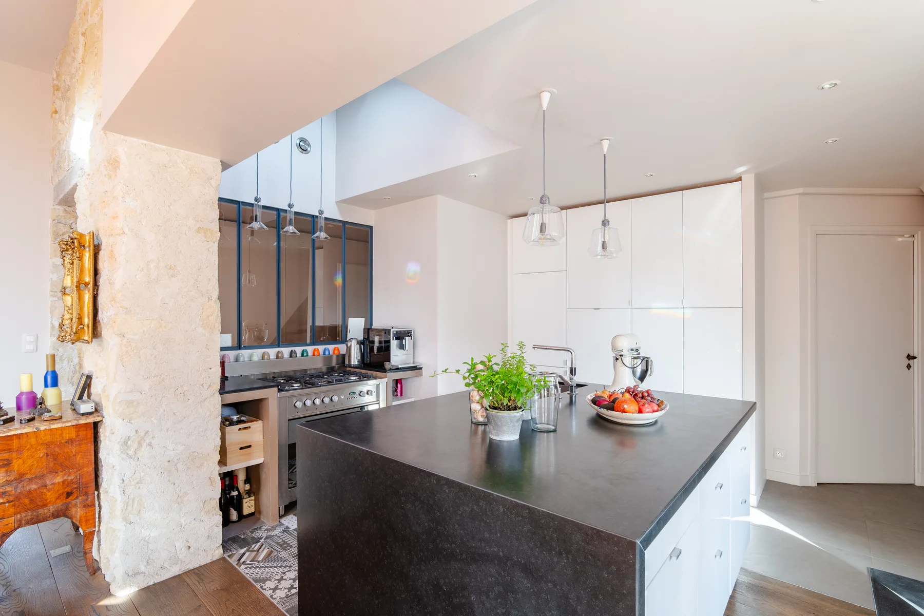 A modern kitchen with a dark island, white cabinetry, and a plant.