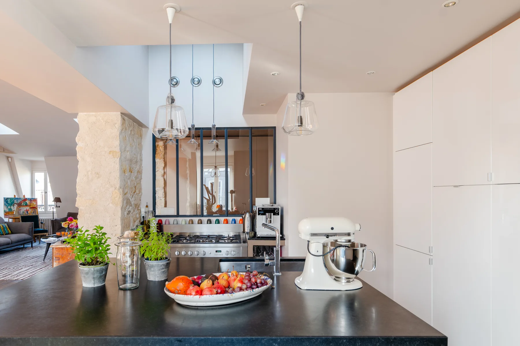 A modern kitchen with a dark island, countertop plants, and a stand mixer.