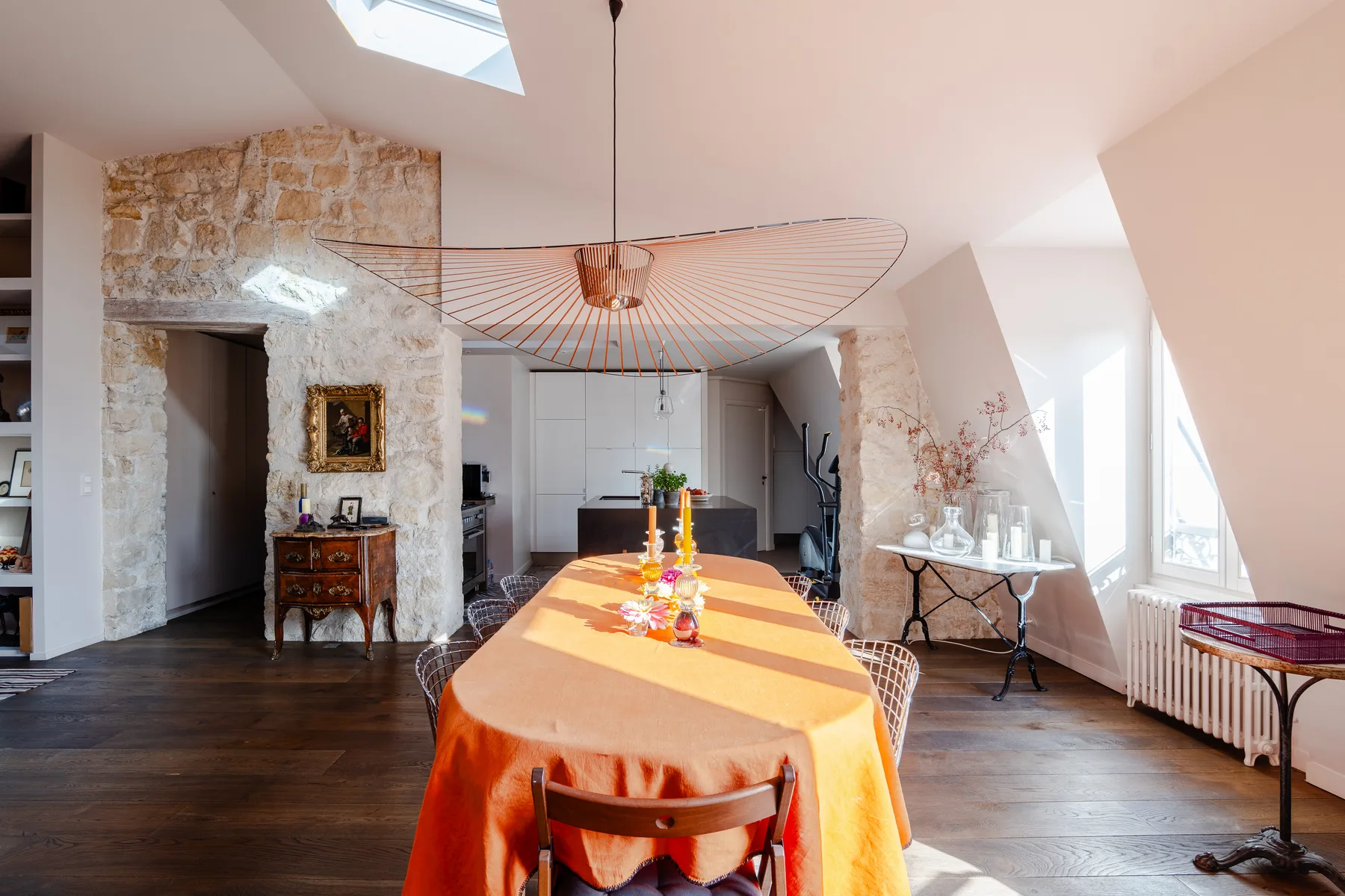 A bright dining area has a long table beneath a sculptural pendant light.