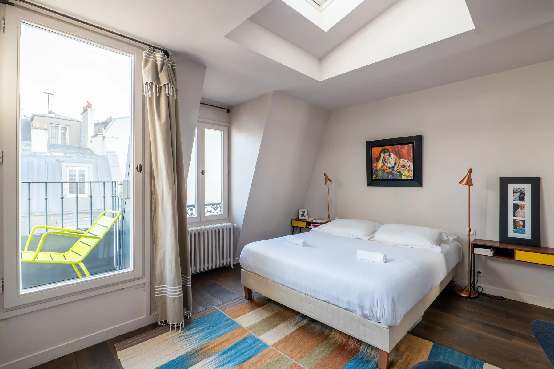 A bright bedroom with a bed, sloped ceiling, and balcony doors.