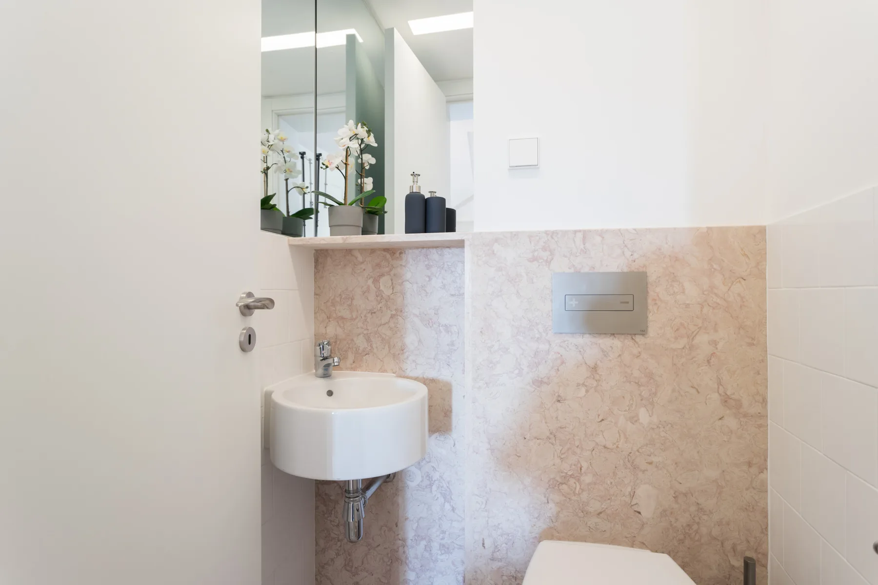 Un baño luminoso con un lavabo de pared y un espejo grande.