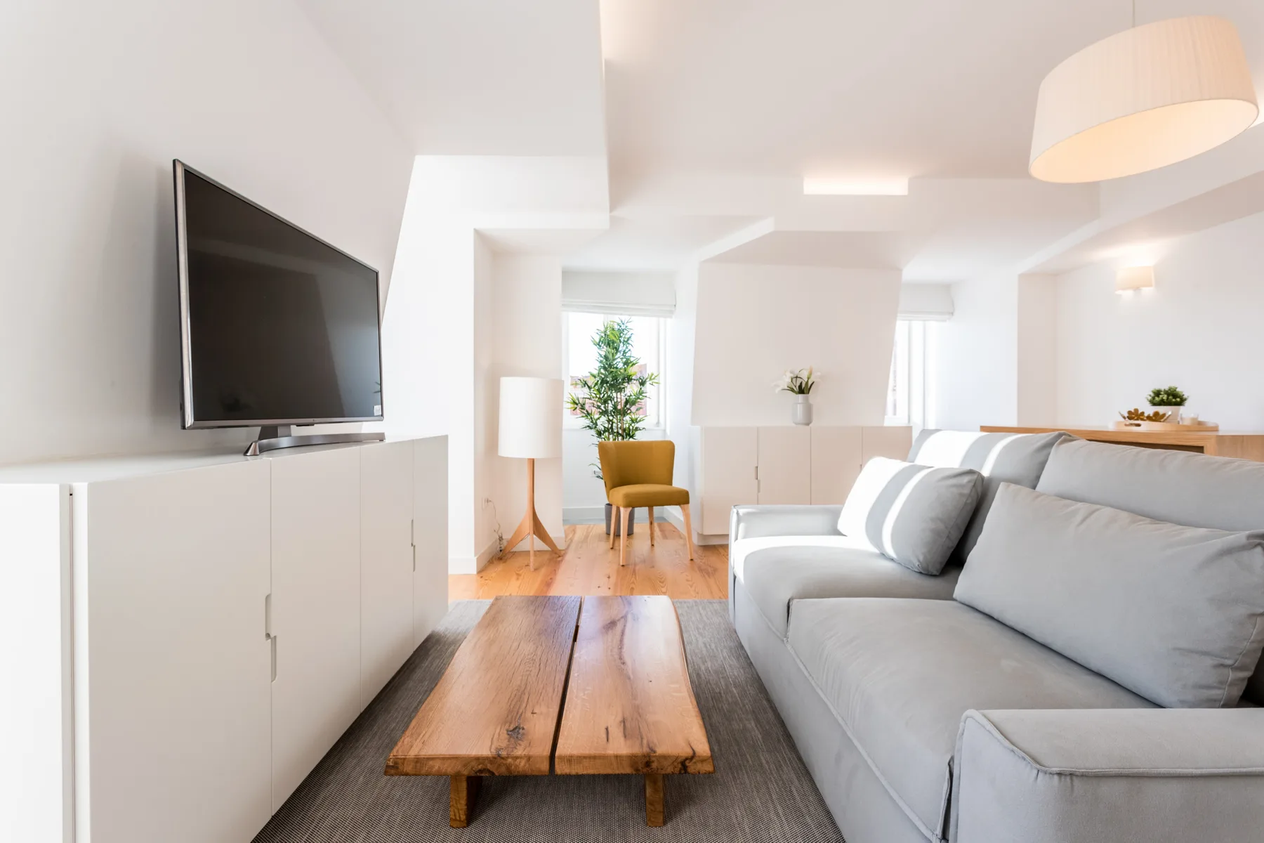 Una sala luminosa con sofá gris, mesa de centro de madera y televisor.