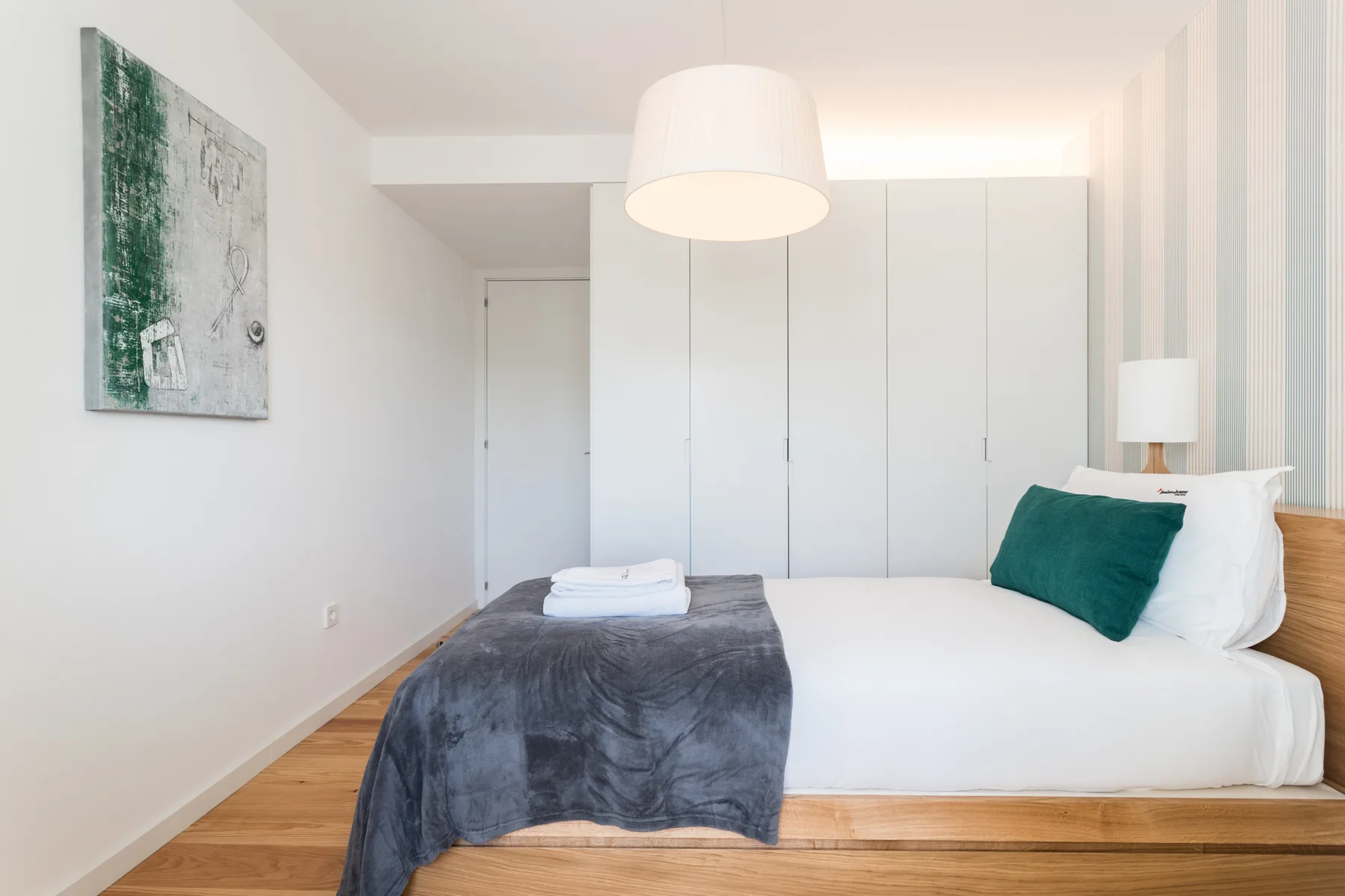 Un dormitorio luminoso con una cama, una lámpara de noche y arte en la pared.