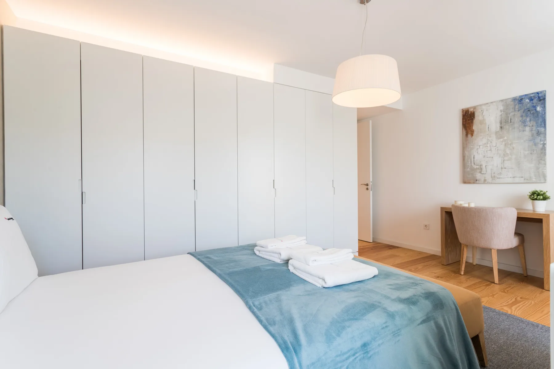 Un dormitorio luminoso con una cama, armarios empotrados y un pequeño escritorio.