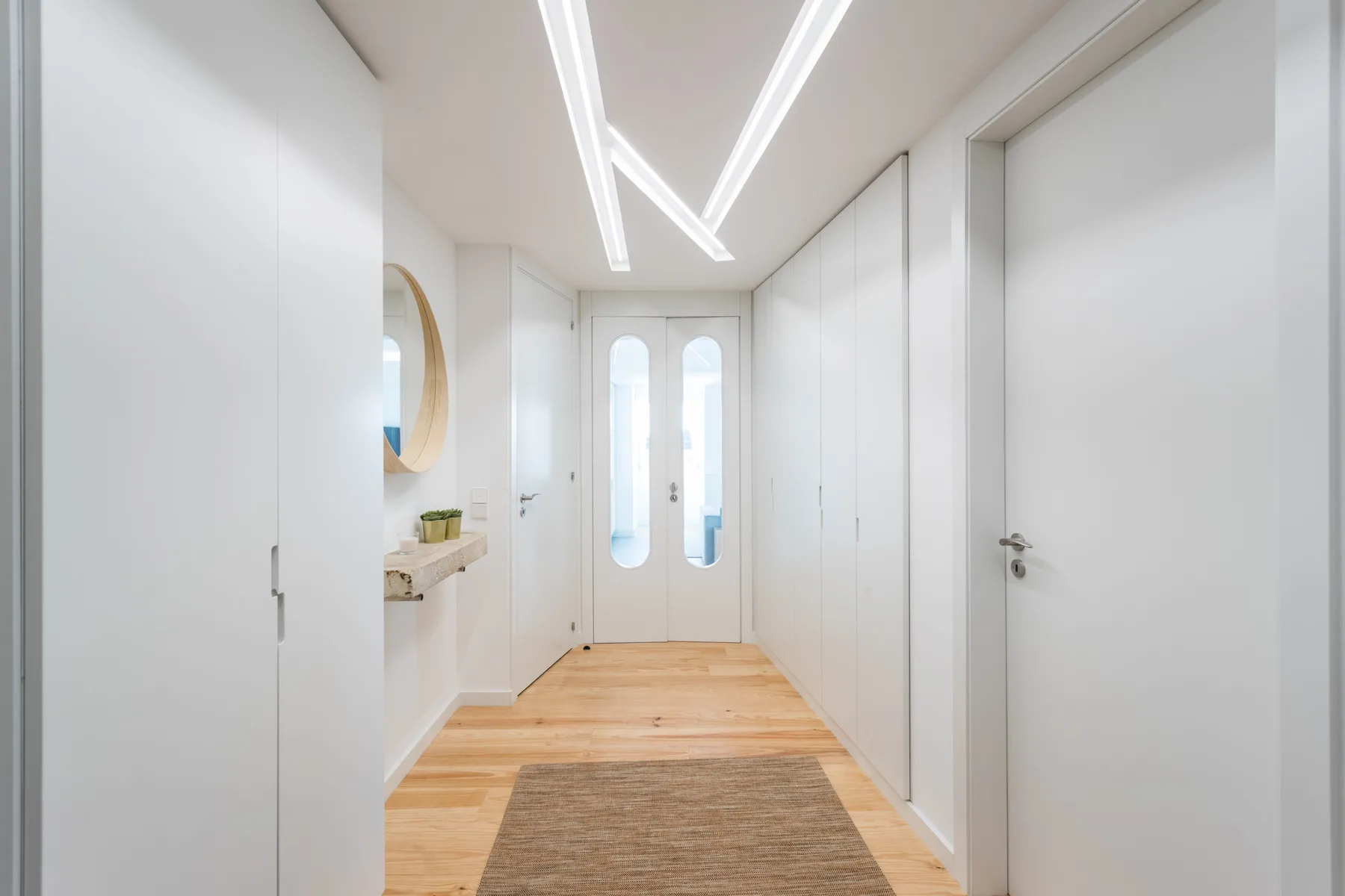 Un pasillo luminoso con armarios blancos, suelo de madera y una alfombra estrecha.