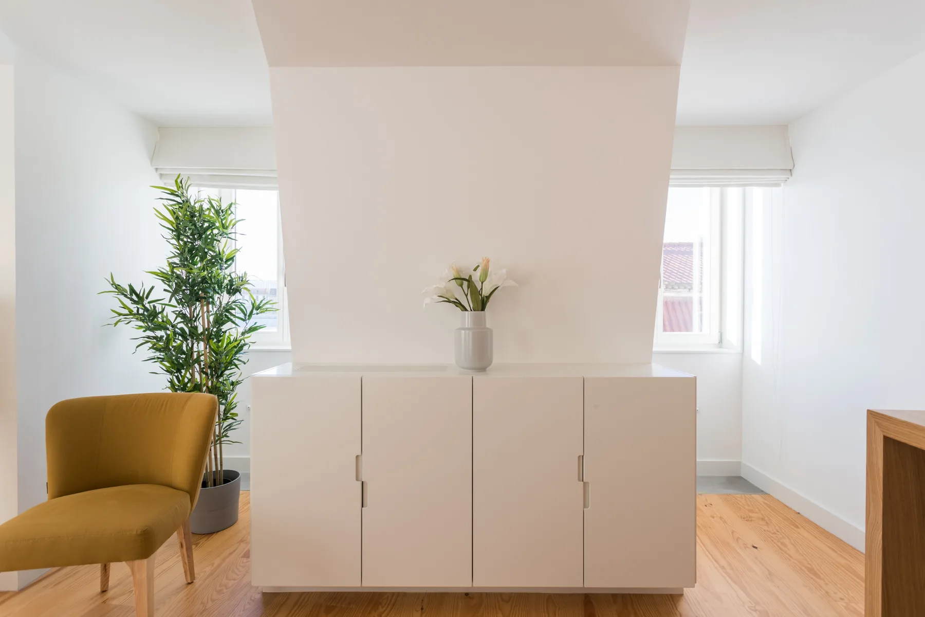 Una habitación luminosa con un mueble bajo, una planta en maceta y asientos color mostaza.