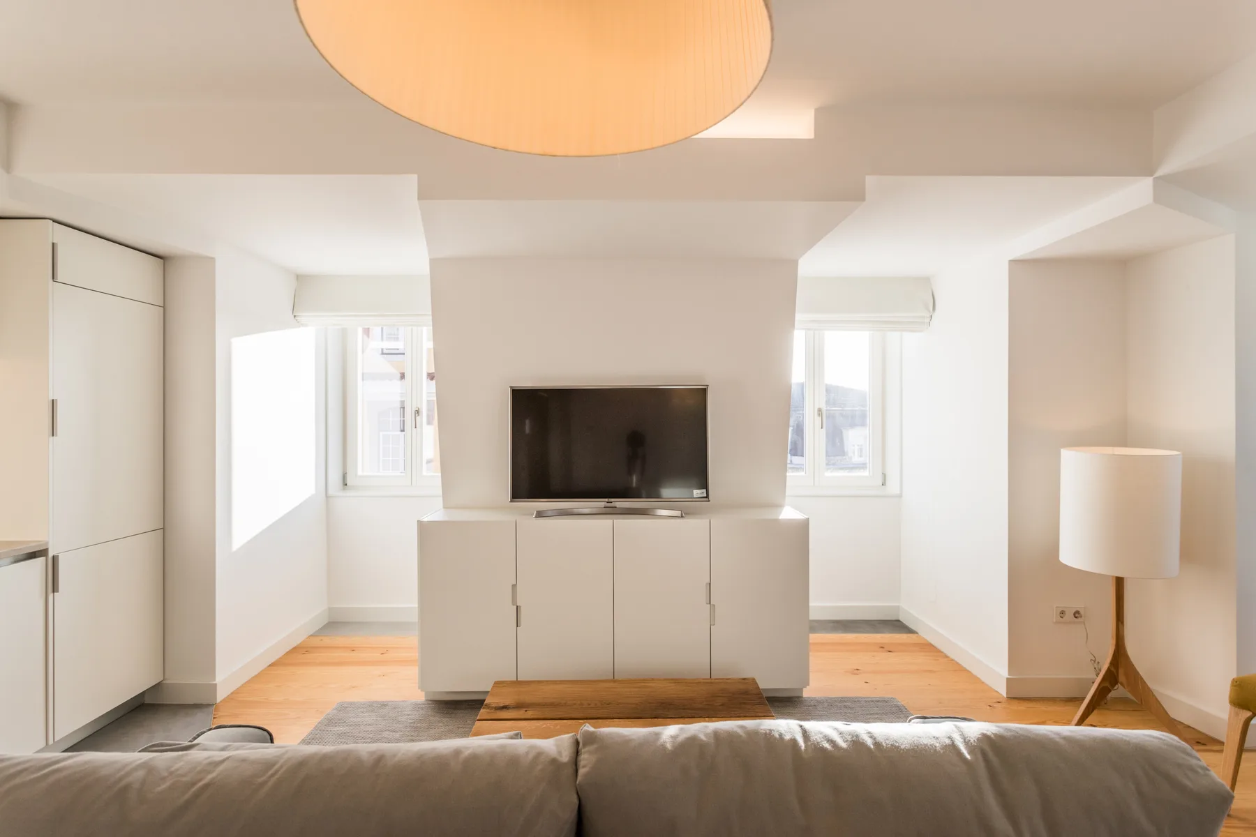 Una sala luminosa con televisor, asientos y ventanas.