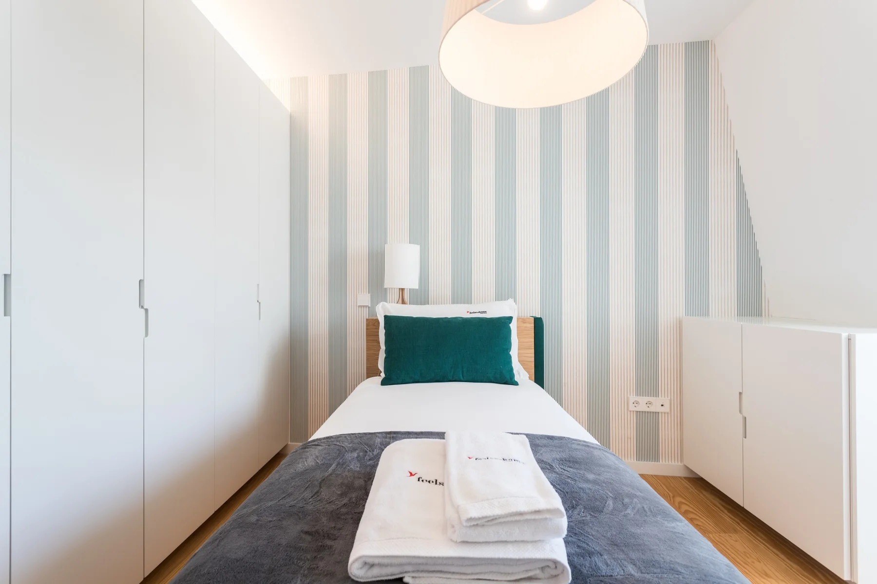 Un dormitorio luminoso con una cama arreglada y papel pintado a rayas.